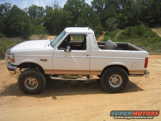 White 1996 Ford Bronco with lifted suspension and side steps parked on a dirt road