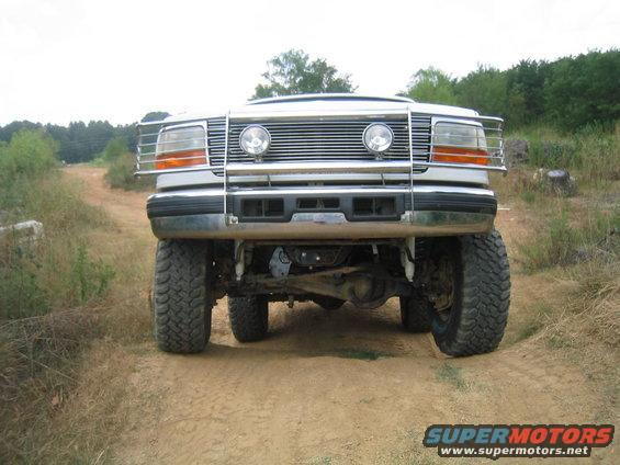 White Ford Bronco with a chrome grille guard and large tires on a dirt road