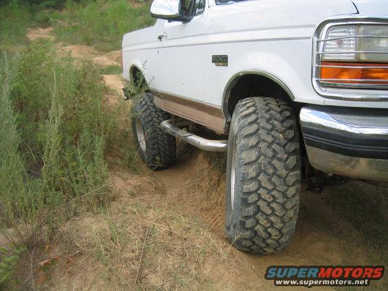 White 1996 Ford Bronco with large off-road tires on a dirt path