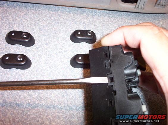hand using screwdriver on car window switch assembly, loose buttons nearby