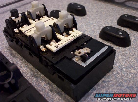 Power window switch assembly with four white actuators and circuit board, separate black button caps nearby