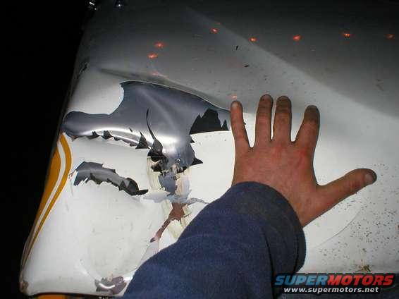 Hand touching severely dented and peeling white vehicle fender with yellow stripe detail
