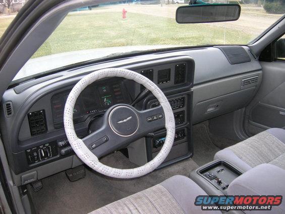 Car interior showing dashboard, steering wheel with white cover, and seats. A fire hydrant is visible through the windshield