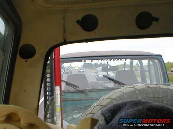 Interior view of a vehicle looking out the rear window at traffic, with a spare tire visible