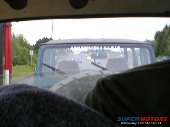 1978 Ford Bronco interior looking out rear window at highway traffic. Decal on rear window reads "BIG BRONCOS 4 X 4 CLUB"
