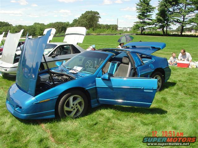 Blue 1984 Pontiac Fiero with doors and hood open, parked on grass