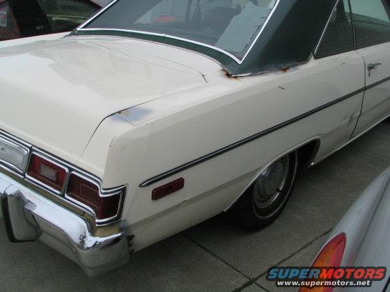 Rear quarter of a white sedan with a green vinyl top. Another car is partially visible in the foreground