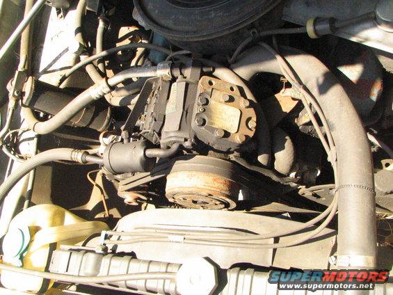 Engine bay showing air conditioning compressor, belts, and hoses. Water reservoir and radiator visible