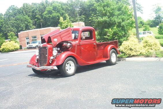 Red hot rod pickup truck with hood open, showing engine. Parked outside