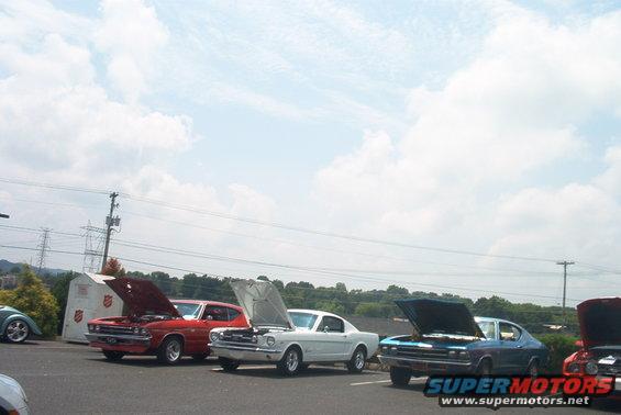 Several classic cars parked outdoors with hoods open