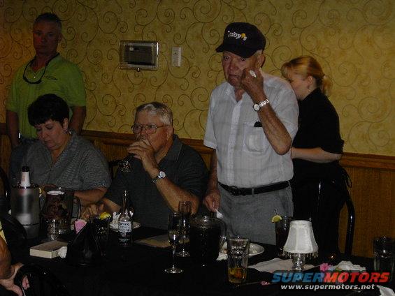 older man in plaid shirt and cap, woman in green shirt, and woman in black shirt at a table with drinks