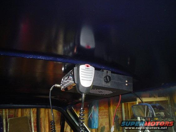 CB radio and microphone attached to the ceiling of a vehicle, with a side mirror visible