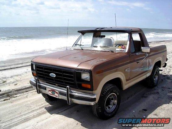 1985 Ford Bronco parked on sand with ocean in background