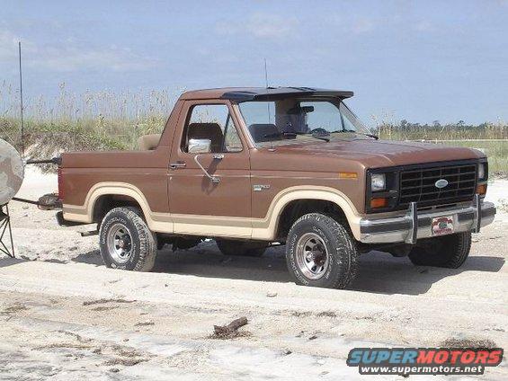 Brown Ford Bronco with tan trim, parked on sand. Visible front grille, headlights, and side profile