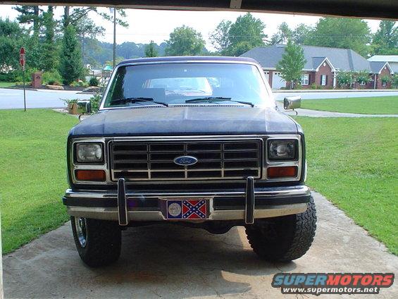Front view of a dark blue 1980s Ford Bronco with a Confederate flag license plate frame