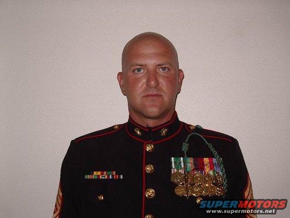 Man in a dark military uniform with medals and ribbons, bald head, facing forward