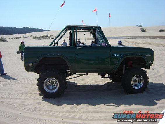Green Ford Bronco with roll cage and large tires parked on sand dunes