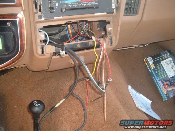 Car interior showing exposed radio wiring, a Haynes manual, and a 4-speed shifter