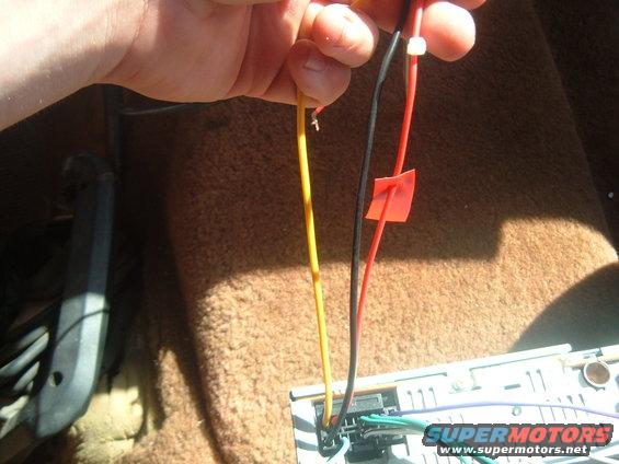 Hand holding yellow and red wires connected to a car stereo's wiring harness