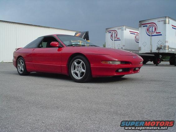 Red 1996 Ford Probe parked on asphalt with trailers in background