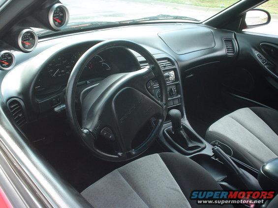 Interior of a 1996 Ford Probe showing dashboard, steering wheel, center console with shifter, and aftermarket gauges