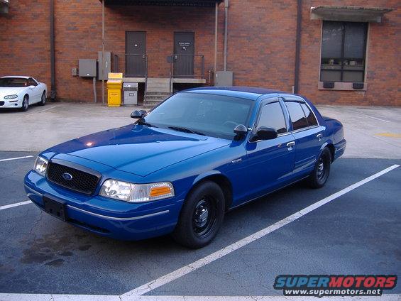 Blue Ford Crown Victoria police car parked, white Chevrolet Camaro in background