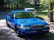 1998 Ford Crown Victoria - A blue sedan with a chrome grille is parked outdoors, with another white car visible in the background.