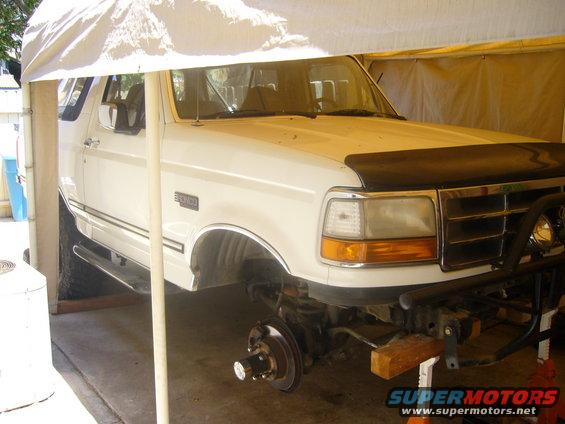 White 1992 Ford Bronco with front suspension removed, parked under a canopy