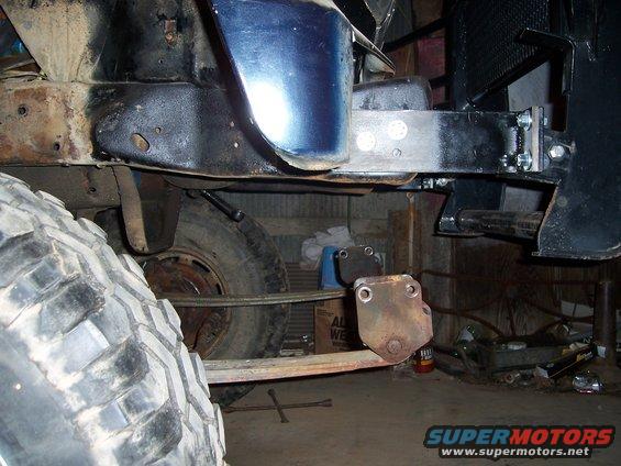 Close-up of vehicle frame, leaf spring, and large tire. Some parts are painted black, others show rust