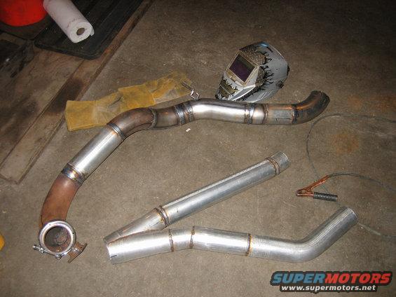 Welding mask, gloves, and custom exhaust pipes laid out on a concrete floor