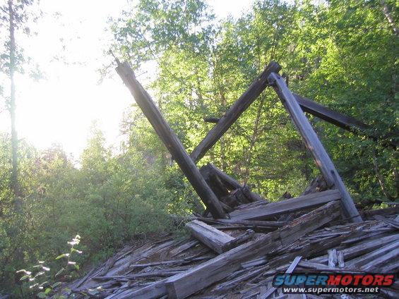 Ruined wooden structure with broken beams and debris in a forest setting