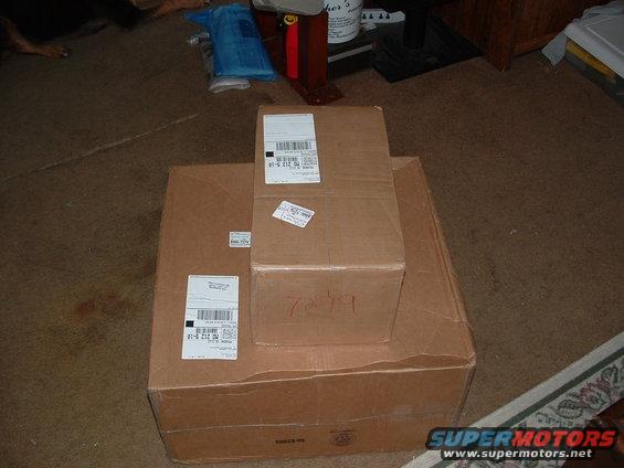 Three stacked cardboard boxes with shipping labels and handwritten markings on a carpeted floor