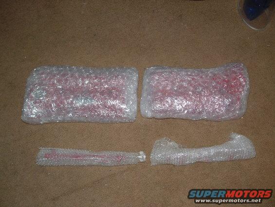 Four red car parts wrapped in bubble wrap on a brown carpeted surface