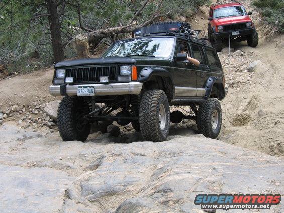 Green Jeep Cherokee on rocks, red Jeep Cherokee behind it on a trail