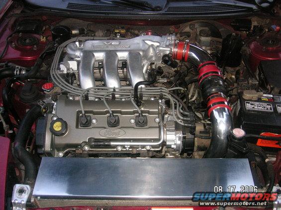 Engine bay with a V6 Ford engine, intake piping, and battery