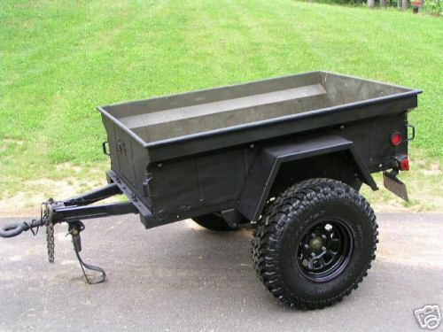black trailer with off-road tires, parked on asphalt with grass in background