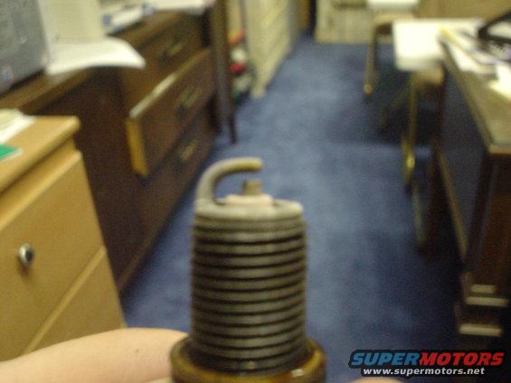 Close-up of a used spark plug held in a hand, with office furniture in the background