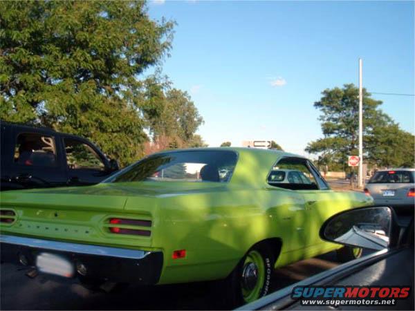 Lime green 1970 Plymouth Road Runner coupe, rear view, parked next to a black truck and a silver sedan