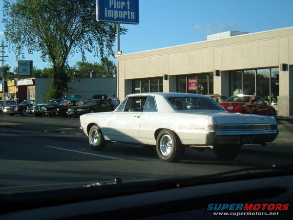 White coupe with chrome wheels, seen from the rear quarter