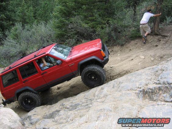 Red 1996 Jeep Cherokee climbing a rocky incline with a person on the side