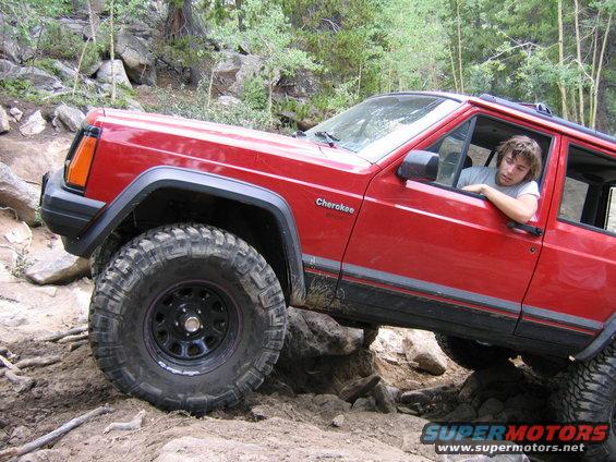 Red 1996 Jeep Cherokee navigating rocky terrain with driver visible