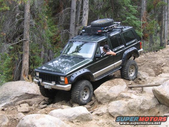 Green 1996 Jeep Cherokee on a rocky trail with a spare tire on the roof rack