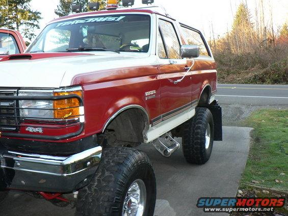 Red and white lifted Ford Bronco with off-road tires and a "4x4" badge