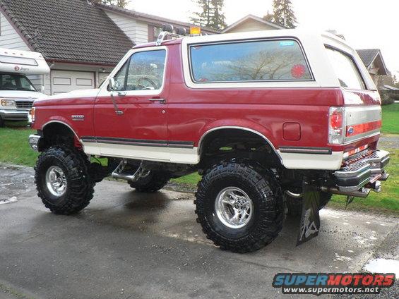 Lifted red and white 1989 Ford Bronco with large off-road tires parked in a driveway