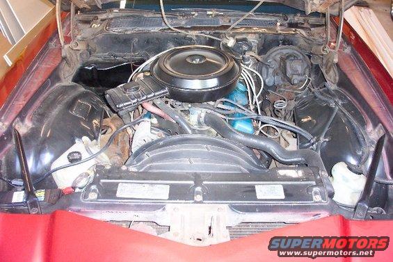 Engine bay of a red car with a black air cleaner and blue engine block, viewed from above
