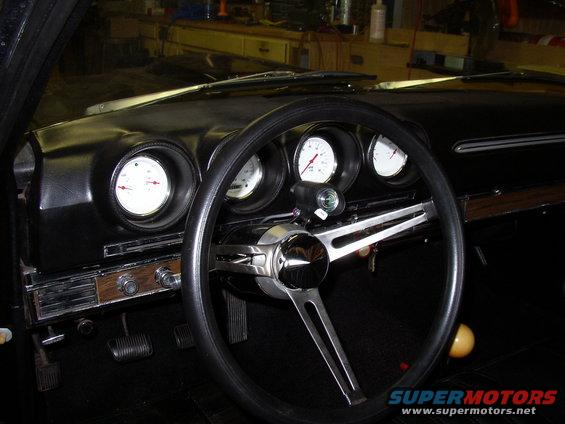 Dashboard of a 1969 Ford Ranchero with three gauges, a black steering wheel, and wood-grain trim
