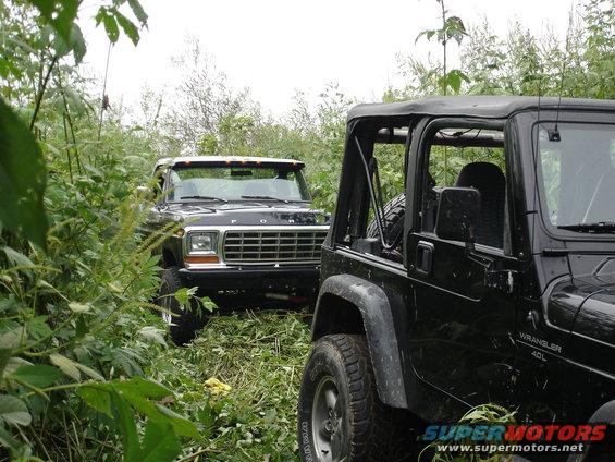 1979 Ford Bronco and a black Jeep Wrangler parked in tall grass