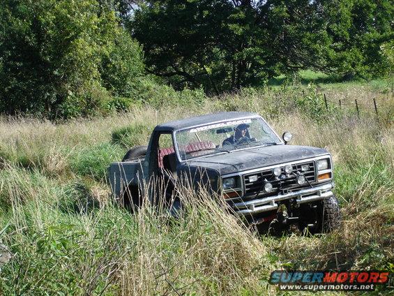 1979 Ford Bronco 3q-front view, dark color, off-road in tall grass