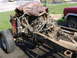 1978 Ford Bronco - The chassis and engine of a vehicle are visible, partially covered by a tarp, with a red vehicle in the background.