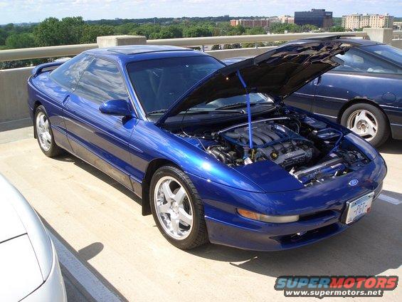 Blue 1993 Ford Probe with hood open, showing engine. Parked on a concrete surface